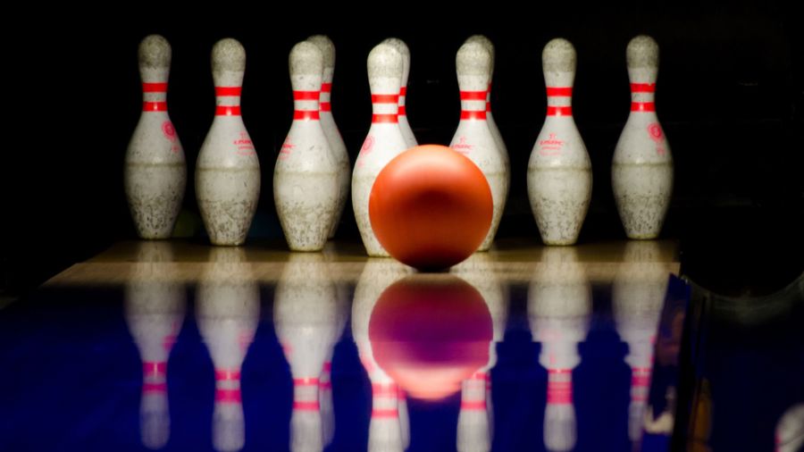 En rad med bowlingkäglor mot svart bakgrund. Framför syns ett rosa bowlingklot.