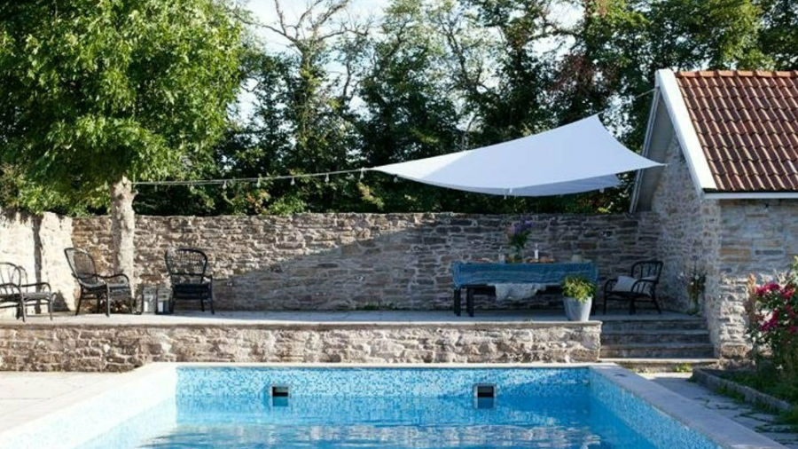 Pool med stenläggning runtom, en stenmur samt gröna träd i bakgrunden