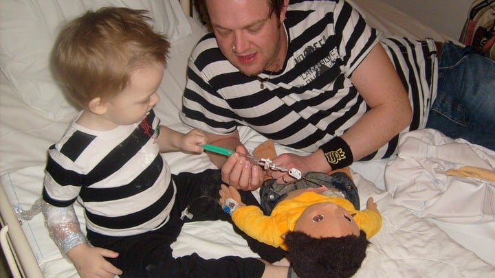 Noel och pappa Henrik ger en docka en spruta i sjukhussängen, foto.