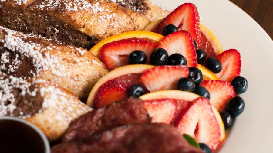 Närbild på en tallrik med apelsin, jordgubbe och blåbär samt skivor av French toast.