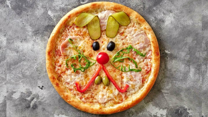 En pizza med ett kaninansikte gjort av grönsaker.