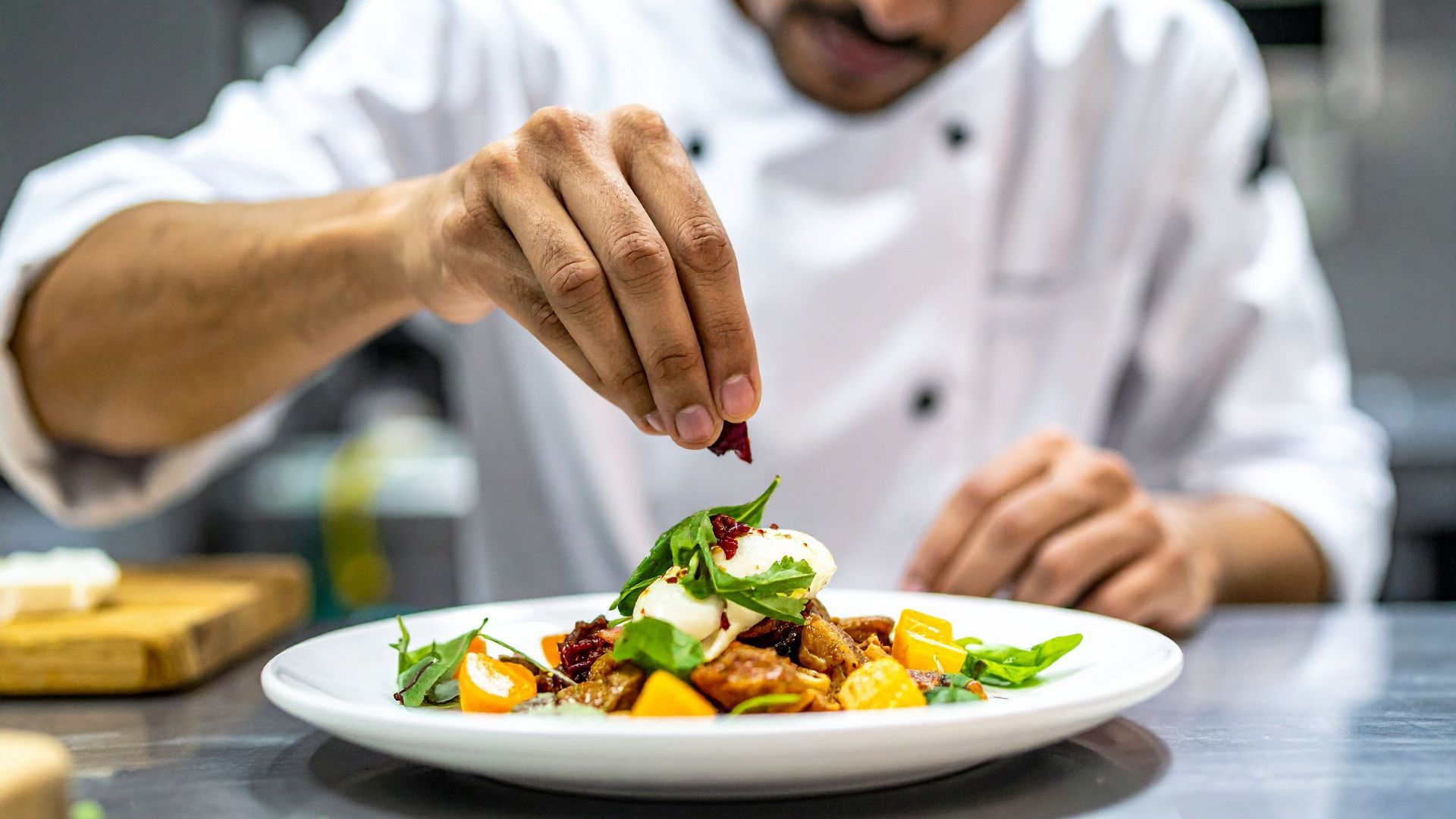 En hand lägger på de sista detaljerna på en tallrik i restaurangkök