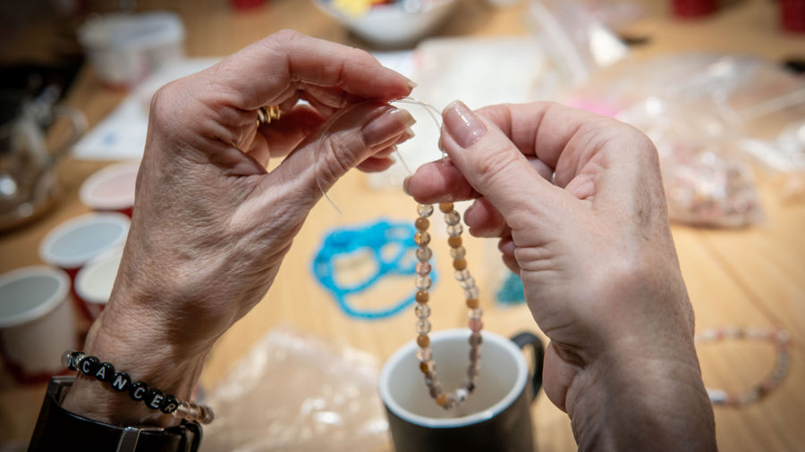 Ett par händer håller i ett snöre som denne trär pärlor på.