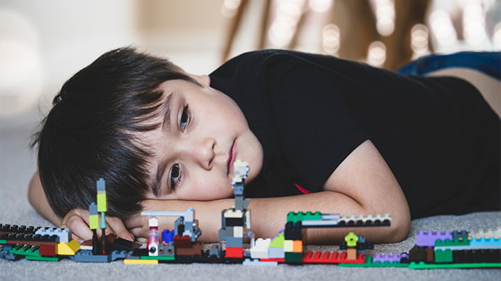 En liten pojke som ligger p&aring; golvet framf&ouml;r Lego