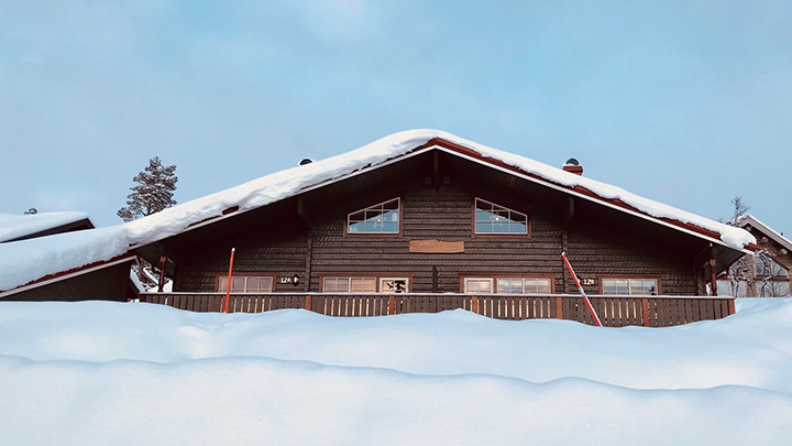 Gråmålad fjällstuga inbäddad i snö