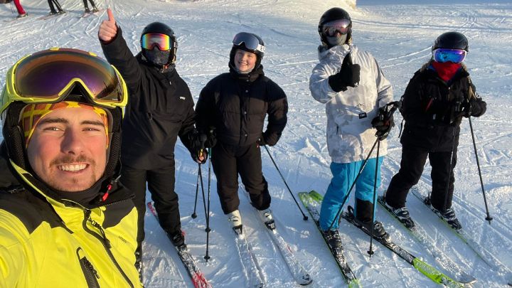 Fem personer som står på skidor och gör tummen upp