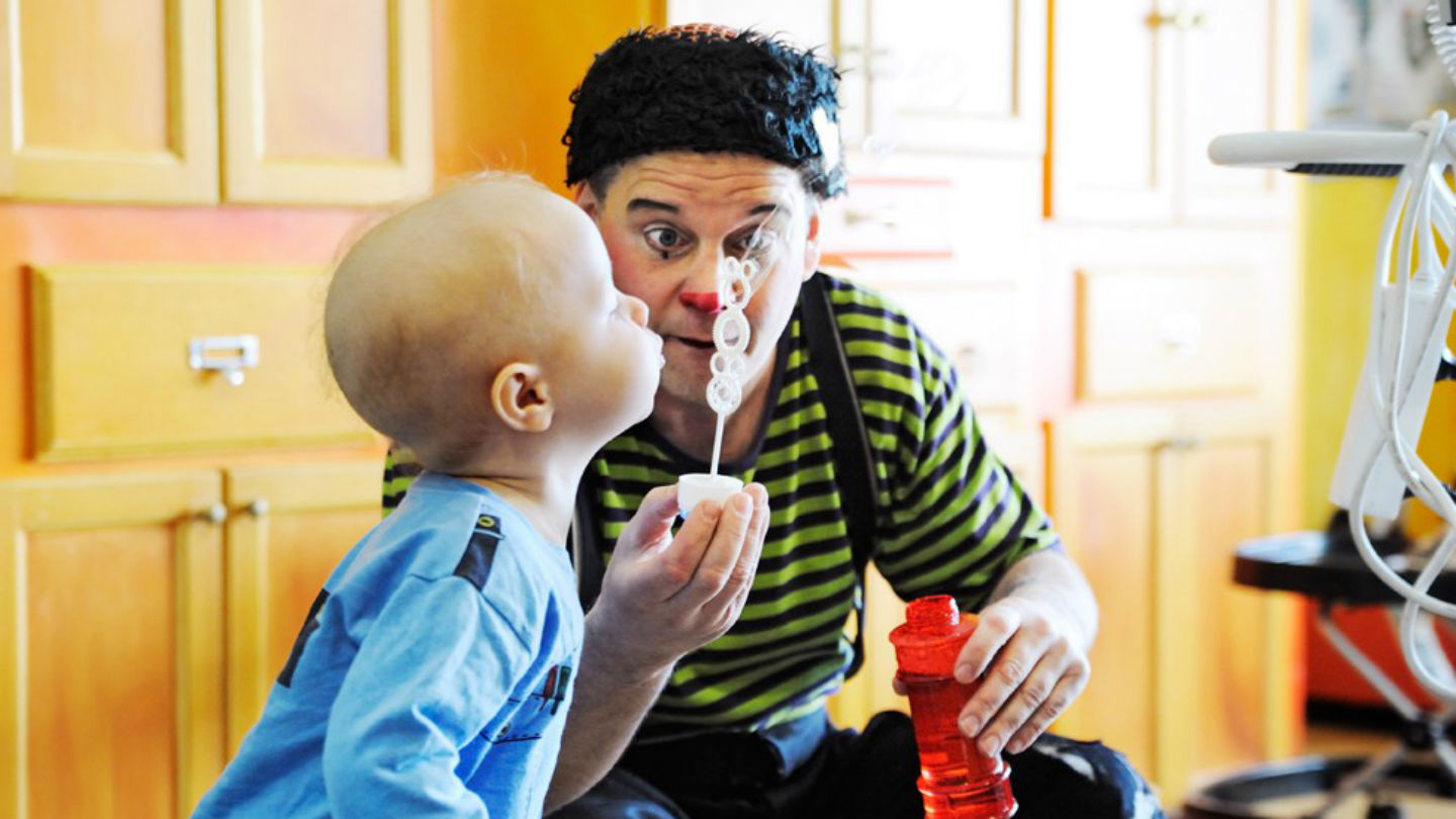 En clown hjälper ett barn blåsa bubblor.